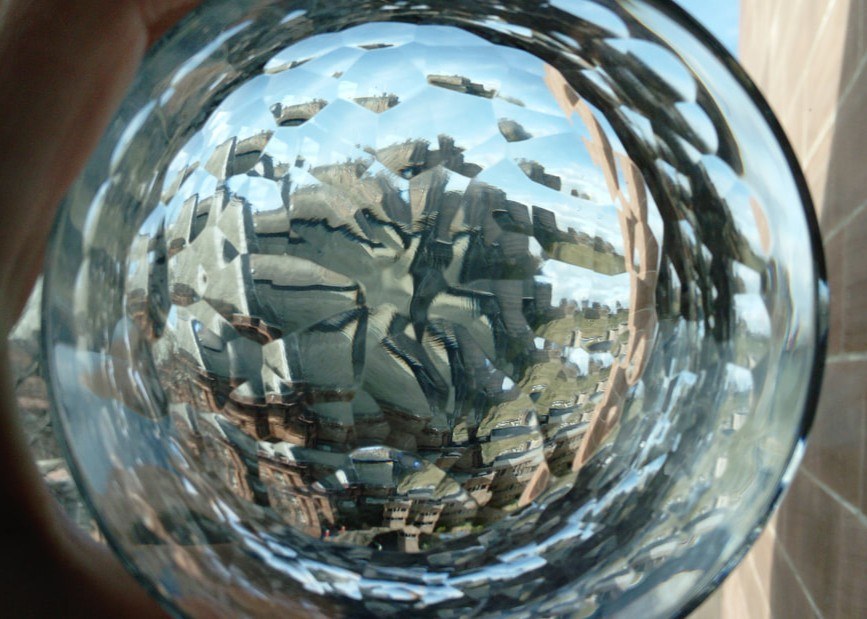 Cut crystal vessel held to the light, rooftops and sky fractured through the facets
