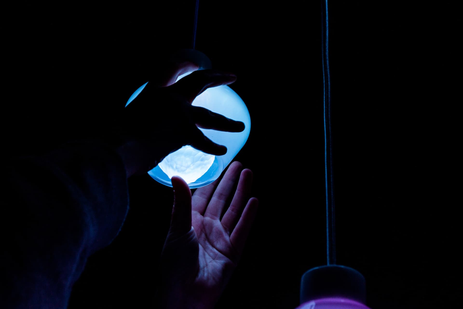 Jewel Lamps — two hands cupping a glowing pendant light in the dark