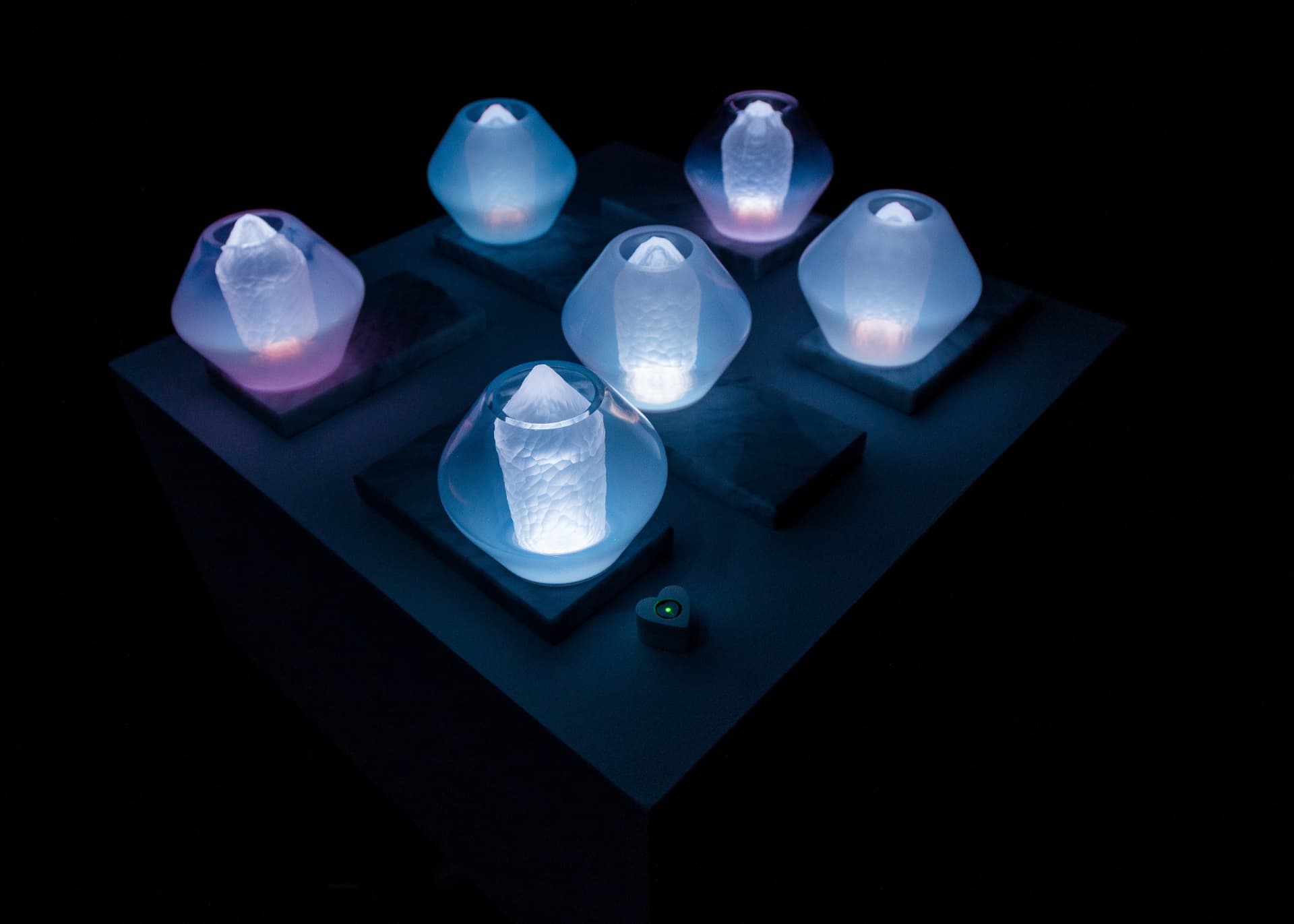 Jewel Lamps — six illuminated table lamps arranged on a plinth with the heart-shaped sensor